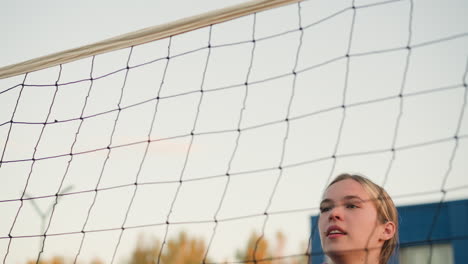 primer plano de una joven atleta que salta, preparándose para golpear el voleibol con enfoque y determinación, mostrando la victoria, la red de voleibol en el fondo y los edificios visibles en la distancia