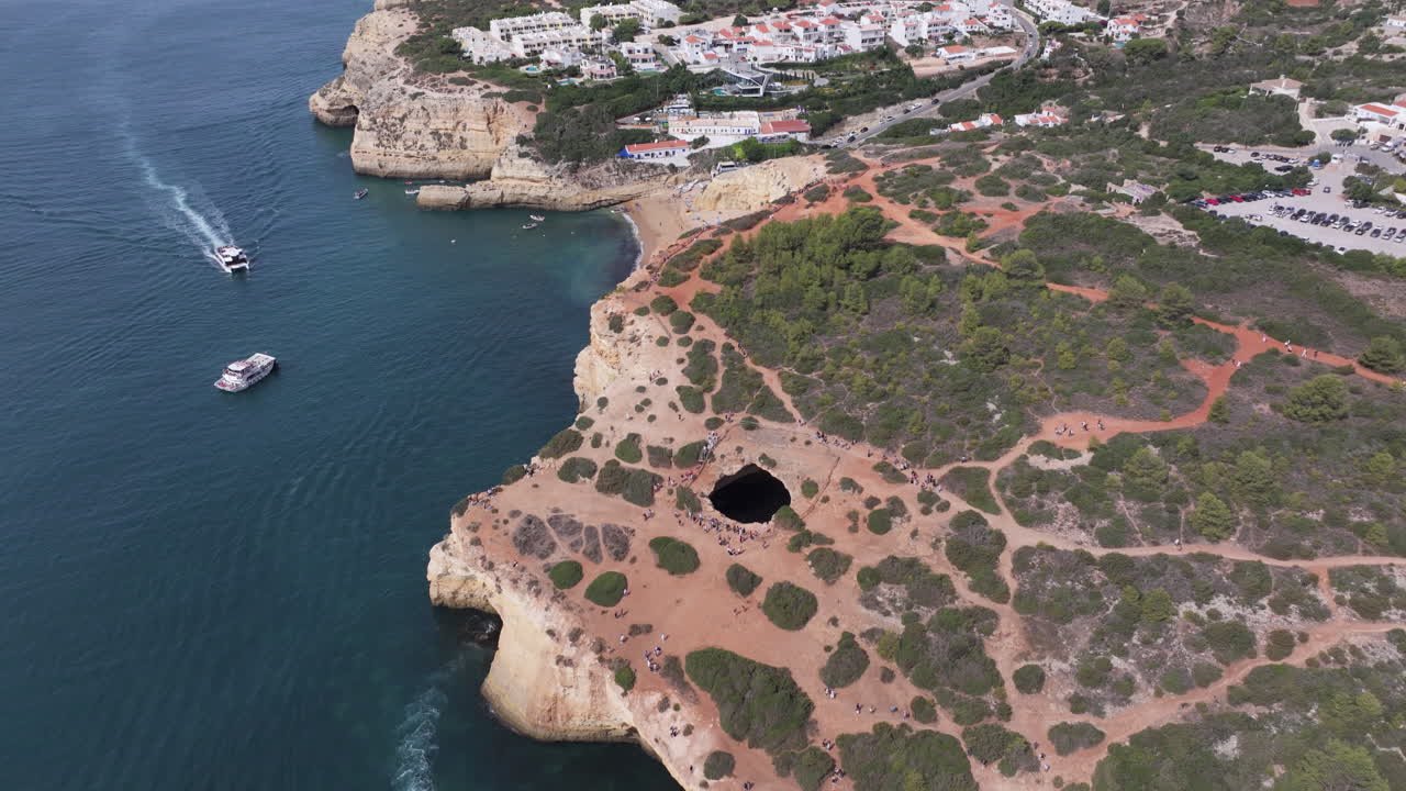 Aerial drone view of the Benagil Sea Cave and Atlantic Ocean coastline in Algarve, Portugal, Europe. Boats, kayaks and tourists. Mass tourism and overtourism concept