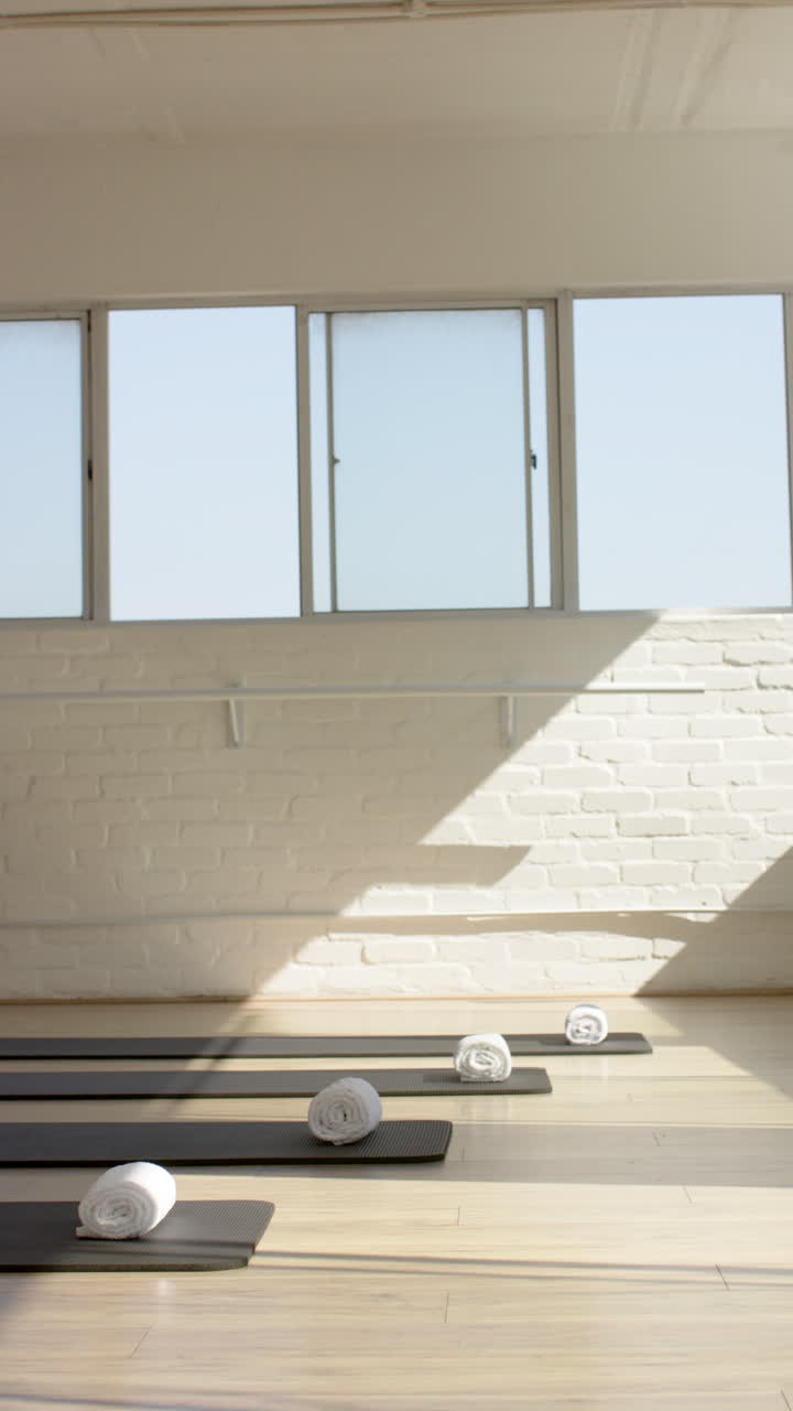 Vertical video: Yoga mats and rolled towels neatly arranged in bright Pilates studio, copy space