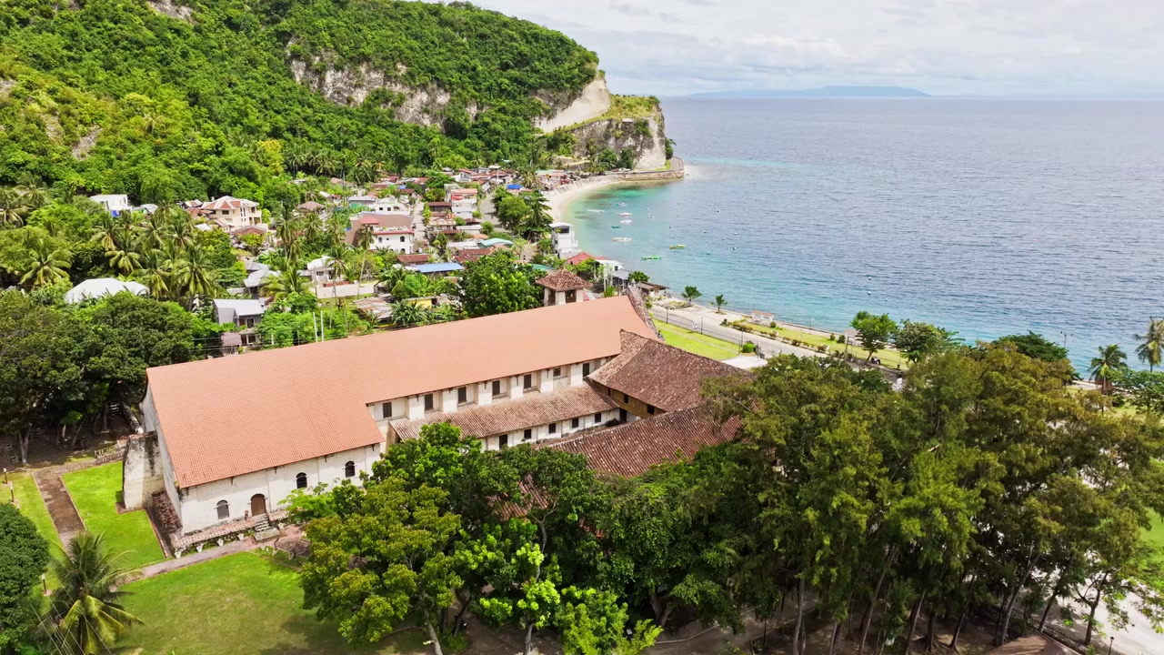 Drone si sposta a destra rivelando la Chiesa di Boljoon in riva al mare nel paesaggio di Cebu, Filippine.