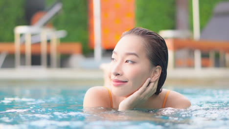 Encantadora-Mujer-Asiática-Relajándose-En-La-Piscina-Sosteniendo-La-Cara-Con-La-Mano