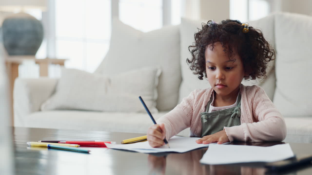 A young girl draws on a piece of paper at a table in a living room