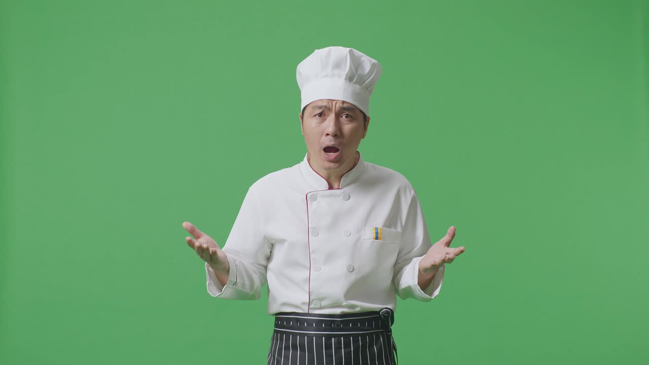 "아시안 남자 요리사는 ""왜?""라고 묻고, 초록색 스크린의 배경 스튜디오에서 의심스럽게 서 있습니다."