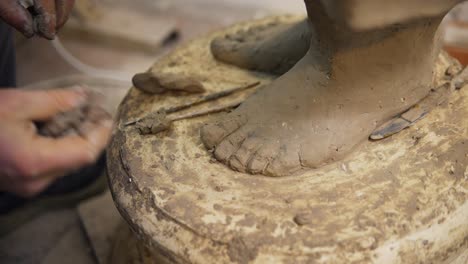 Close-up-of-clay-Buddha's-statue-feet,-artist-works-with-detail-using-tools