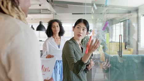 happy diverse casual business colleagues making notes on wall, brainstorming in office, slow motion