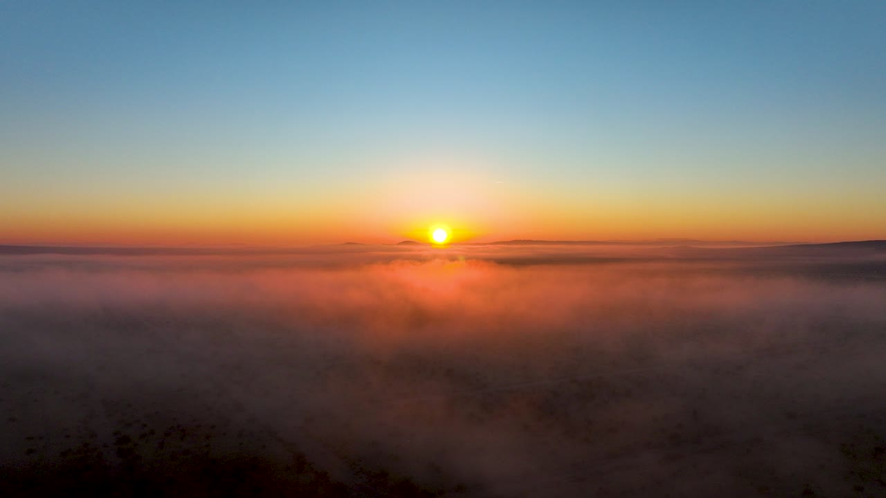 Sunrise over a sea of clouds with warm hues gracing the horizon, aerial