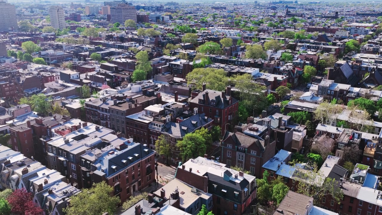 Vista aerea con drone di un quartiere storico di case a schiera di Filadelfia, caratterizzato da tetti vari, architettura vittoriana in mattoni, campanili di chiese e alberi primaverili.