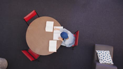 Asian-female-student-wearing-a-blue-hijab-sitting-at-a-round-table-and-reading-a-book