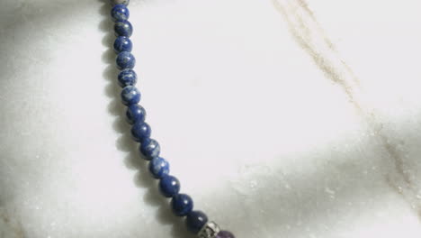 macro dolly shot of blue lapis lazuli beads from a tibetan prayer mala resting on white marble slab shot in uhd