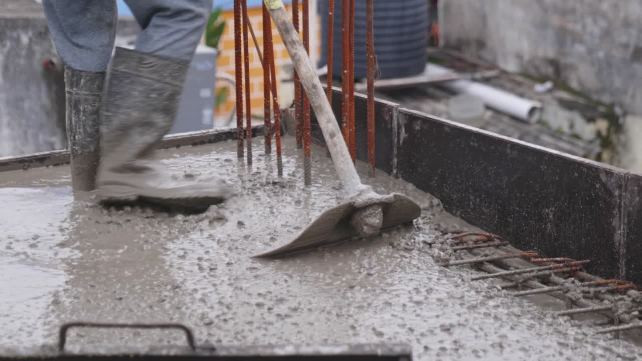 Worker Spreading Wet Concrete with shovel tool and safety boots on Building Slab at construction site. day time, zoom out shot, 4k