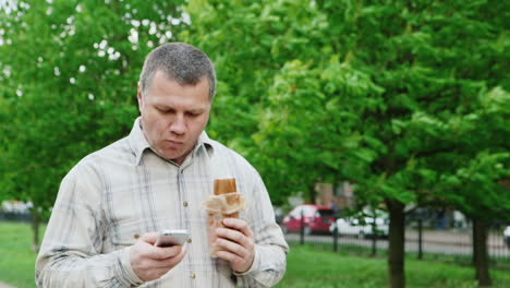 brutal middle-aged man walks down the street there is a fast food uses your smartphone