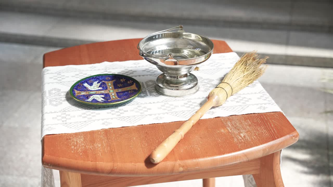 Holy water set with a silver vessel, brush, and decorative plate placed on a white cloth-covered wooden table inside a church, ready for use in a religious ceremony or blessing