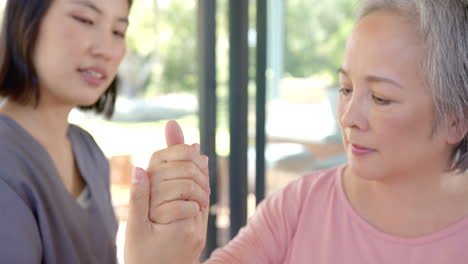 senior asian woman receiving physical therapy, therapist assisting with hand exercises