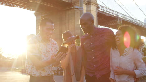 friends look at photos on phone by brooklyn bridge in new york