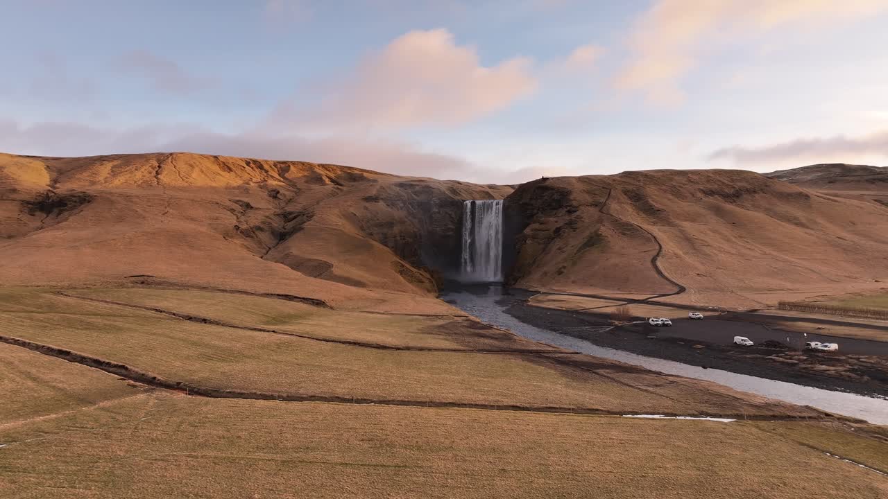 Drone push-in to Skógafoss waterfall in Iceland with golden cliffs and river.