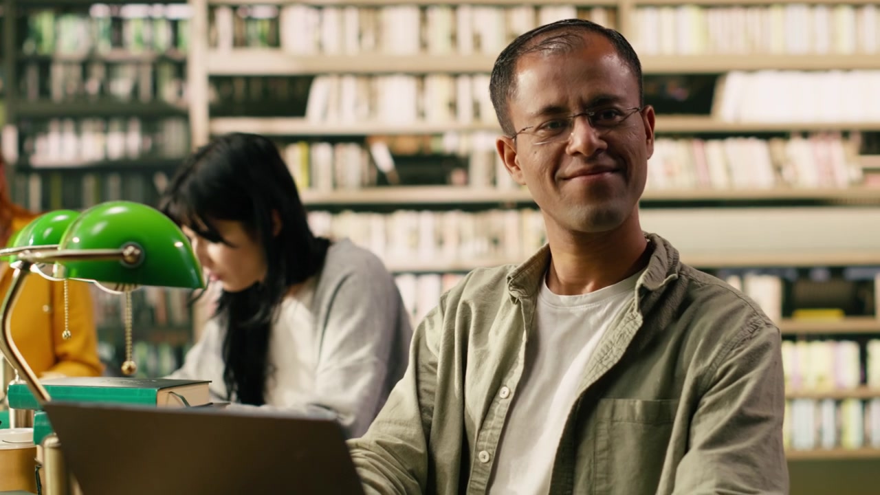 Smiling adult student looks away from laptop in quiet library study area