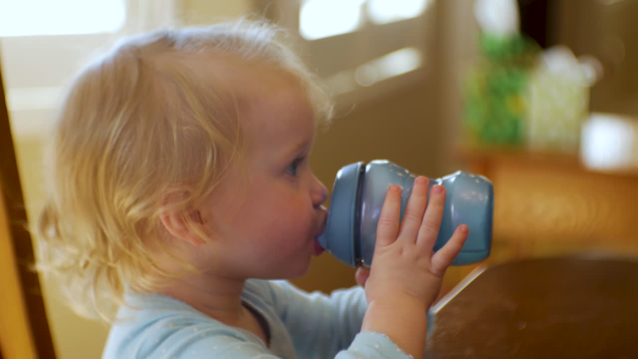 una adorable niña pequeña bebe agua, alegría o leche de su vaso para sorber, de cerca