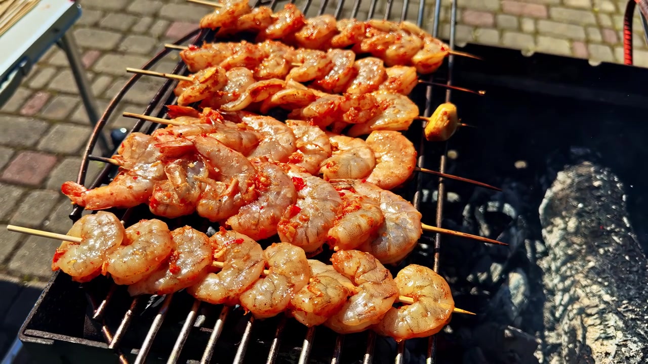 Spiedini di gamberi che grigliano su un barbecue a carbone all'aperto in una giornata di sole