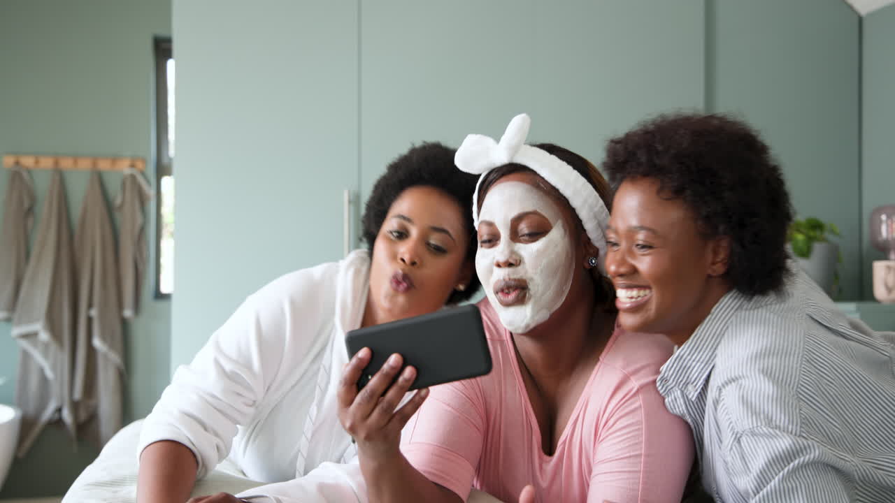 Donne afroamericane che si fanno un selfie insieme, sorridono e si godono una giornata spa a casa.