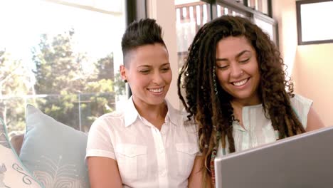 pareja feliz de lesbianas usando computadora portátil juntos en el sofá