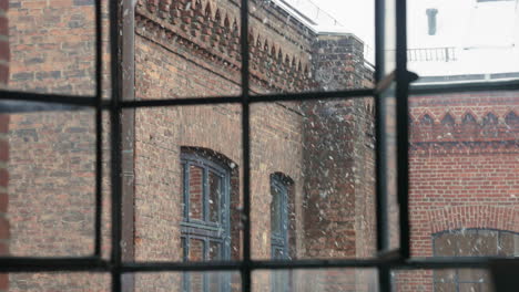 Man-opening-vintage-window-and-gazes-out-a-snow-dappled-window-overlooking-a-brick-building