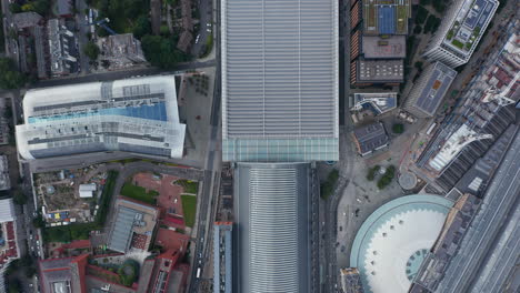 Aerial-birds-eye-overhead-top-down-panning-view-of-buildings-in-city.-Large-roof-of-St-Pancras-train-station-and-following-railway-track.-London,-UK