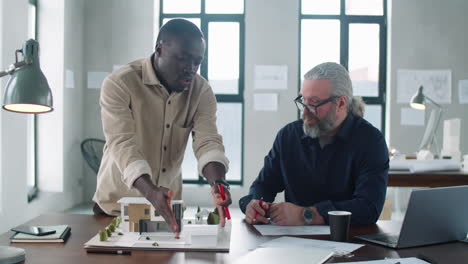 arquitecto negro discutiendo el modelo de construcción con un colega sénior