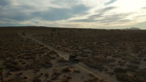 Vista-Aérea-De-Un-Vehículo-Todoterreno-Que-Conduce-A-Lo-Largo-De-Un-Sendero-Polvoriento-Del-Desierto-Al-Atardecer