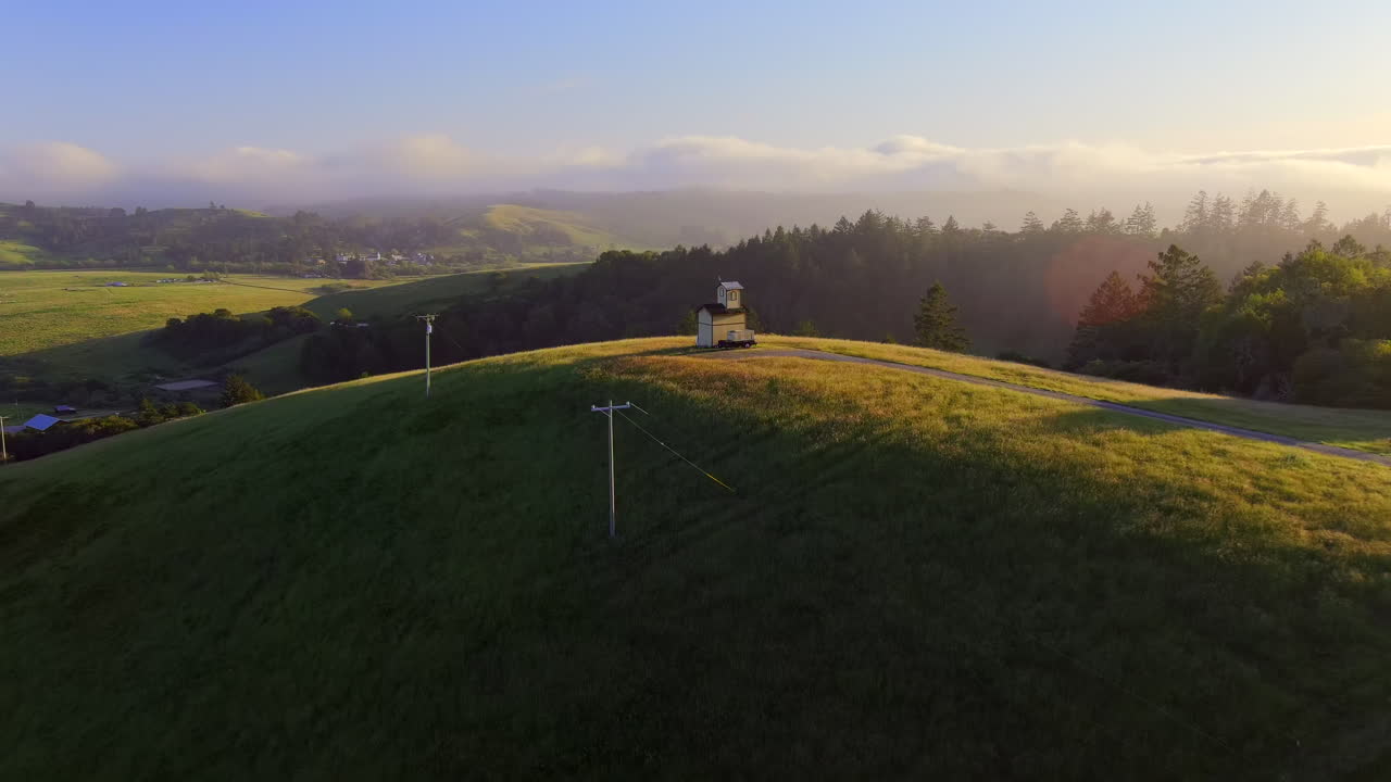 미국 캘리포니아주 소노마 카운티 보데가 근처 안개 낀 오후 동안 초록빛 언덕 위의 고립된 구조물 위를 날다