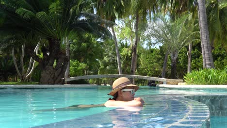 girl wearing a hat and sunglasses relaxing and leaning on the edge of a swimming pool in dos palmas island resort and spa in puerto princesa, palawan, philippines