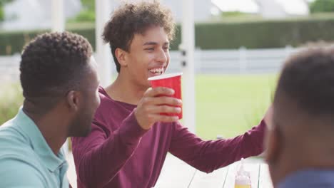 Fröhliche,-Vielfältige-Männliche-Freunde,-Die-An-Sonnigen-Tagen-Im-Garten-Reden-Und-Bier-Trinken