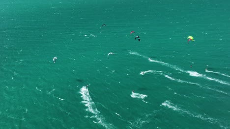 high angle drone - group of kitesurfers flying over ocean surface