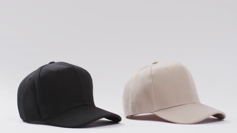 Video-of-black-and-beige-baseball-caps-and-copy-space-on-white-background