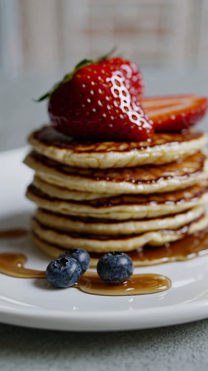Close-up video of a pancake stack topped with strawberries and blueberries, showcasing a delicious