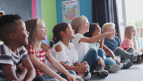 group of laughing elementary school pupils sitting on floor listening to teacher