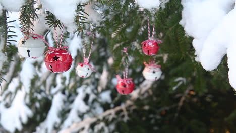 Baubles-hanging-from-spruce-branch-in-snow-swayed-by-wind,-Christmas-tree-decor