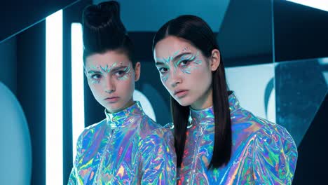 futuristic fashion portrait of two models with iridescent outfits and artistic face makeup under neon lights