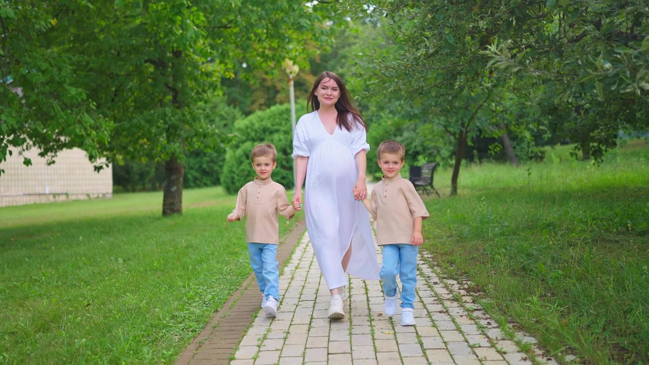 Zwangere vrouw loopt hand in hand met haar twee jonge zoons in een park