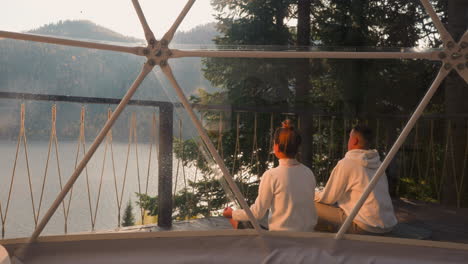 couple meditating in a dome overlooking a lake and mountains at sunrise