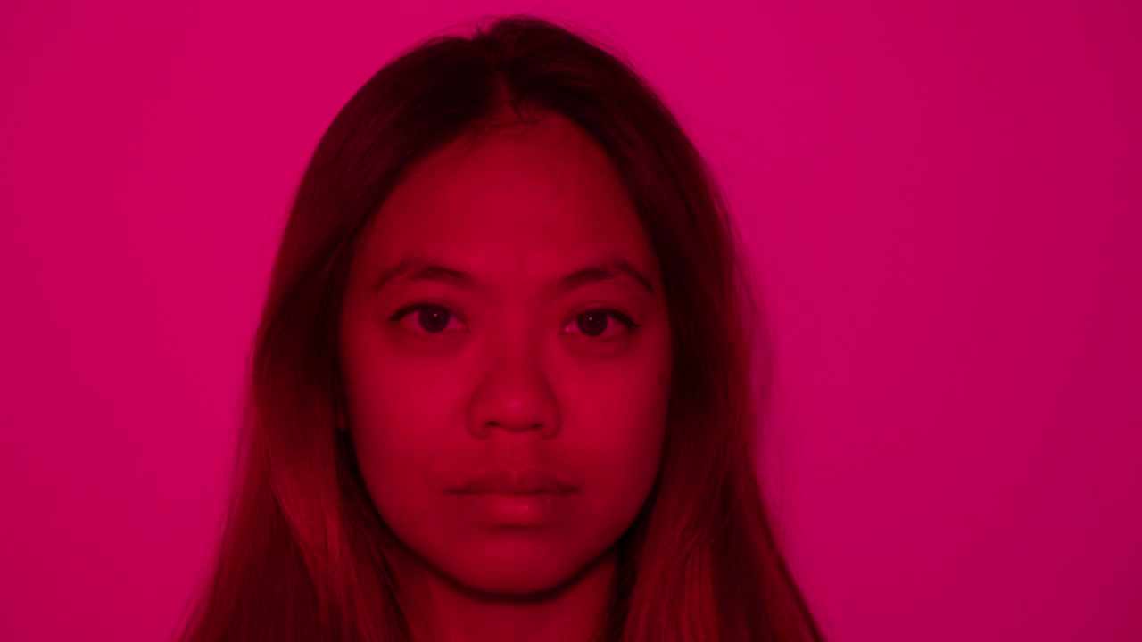 Woman in pink light with reflective expression, soft shadows add depth to scene as light rotates and blossoms deep red to soft pink