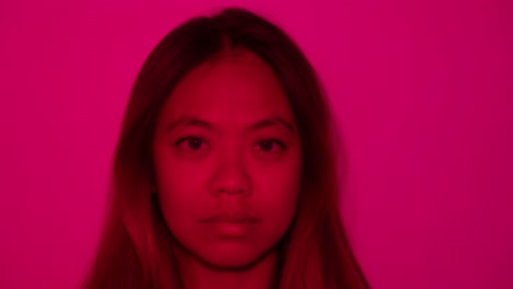 woman in pink light with reflective expression, soft shadows add depth to scene as light rotates and blossoms deep red to soft pink