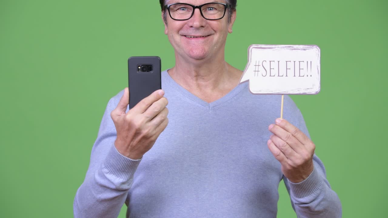 Senior handsome man holding phone and selfie paper sign