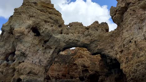 bottom up shot sandstone cliff formation with different caves and peaks at algarve against clouds at sky - tilt down view from boat