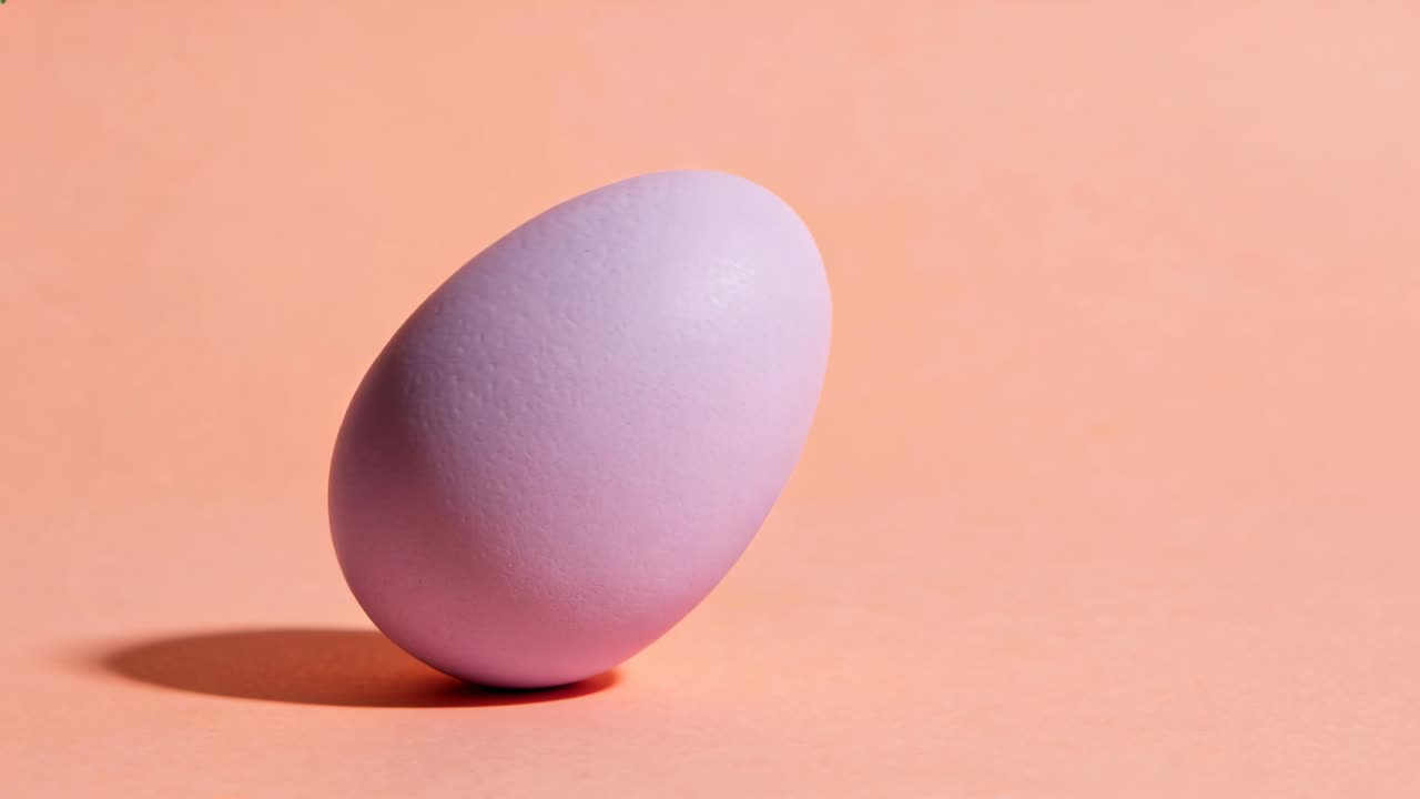 Leaning from imbalance, matte lavender egg tipping, rolling and rocking on peach table with shadow