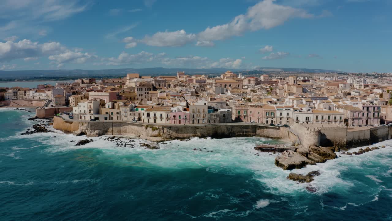 Aerial view of Ortigia island. Old town in Syracuse. Historic architecture on a natural fortress by Mediterranean sea with waves crashing on the coast. UNESCO world heritage site in Sicily.