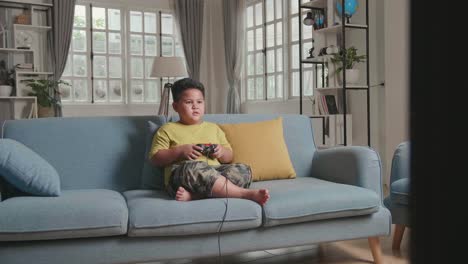 young boy seating on a couch, while playing exited computer game