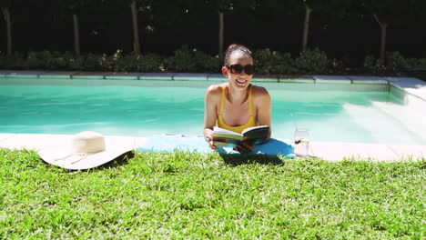 relaxing by pool, woman in sunglasses reading book with refreshing drink nearby, copy space