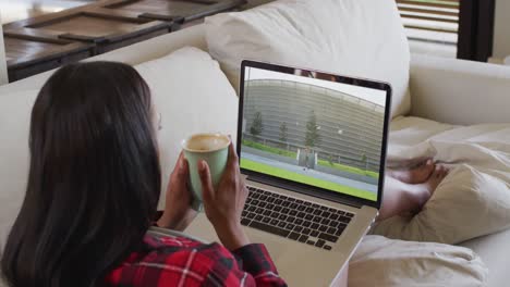 compuesto de una mujer sentada en casa sosteniendo un café viendo un evento de atletismo en una computadora portátil