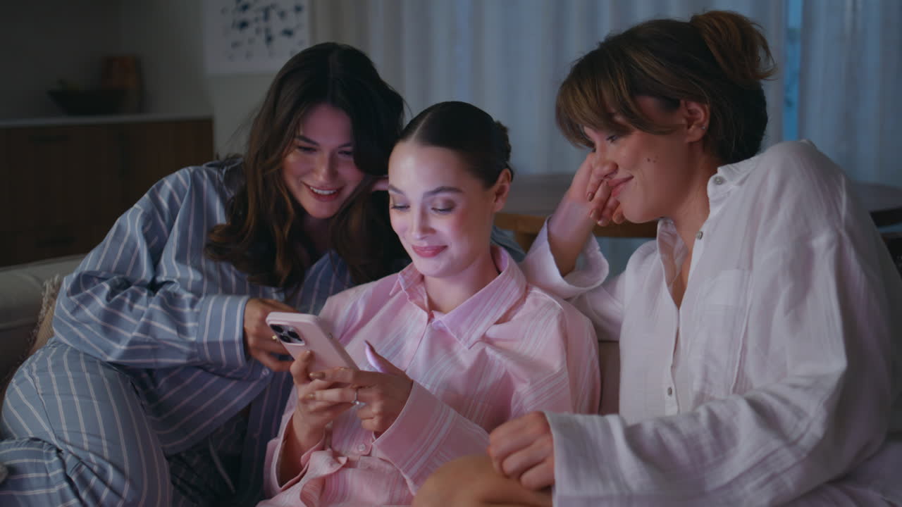 Three women looking smartphone sitting on home couch at girlish meeting closeup