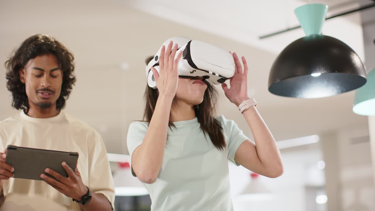 Donna afroamericana che testa un visore VR bianco dopo che un collega ha utilizzato un tablet in un ufficio open space.